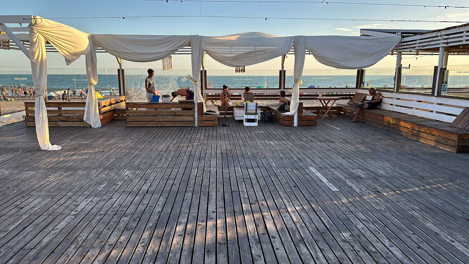 El deck de SHANTI a plena luz, con telas blancas, bancos de madera y el horizonte del mar.